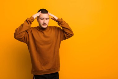 Genç yakışıklı adam konsantre, düşünceli ve ilham verici görünüyor, beyin fırtınası yapıyor ve düz arkaplan karşısında elleri alnında hayal ediyor.