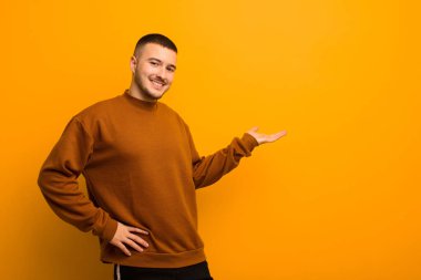 Genç yakışıklı adam gülümsüyor, kendinden emin, başarılı ve mutlu hissediyor, fotokopi odasında düz arkaplan karşısında fikir veya konsept gösteriyor.