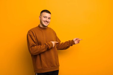 Genç yakışıklı adam gülümsüyor, mutlu, kaygısız ve tatmin olmuş hissediyor, fotokopi alanındaki konsepte ya da fikre işaret ediyor.