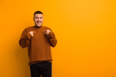 Genç yakışıklı adam mutlu, şaşırmış ve gururlu hissediyor. Heyecanlı, şaşkın bakışlarıyla düz arkaplana bakıyor.