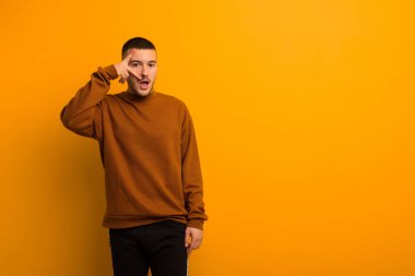 Genç yakışıklı adam şok olmuş, korkmuş ya da korkmuş görünüyor. Yüzü elle kaplanmış ve parmaklarının arasından düz arkaplana bakıyor.