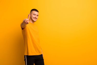 Genç yakışıklı adam gururla gülümsüyor ve gururla bir numaralı pozunu veriyor. Düz arkaplan karşısında bir lider gibi hissediyor.