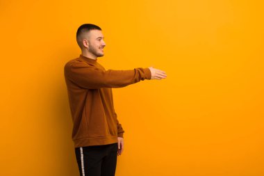 Genç yakışıklı adam gülümsüyor, seni selamlıyor ve başarılı bir anlaşma için el sıkışmayı teklif ediyor.