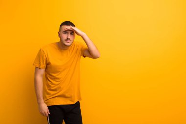 Genç yakışıklı adam şaşkın ve şaşkın görünüyor, el üstünde uzak bakıyor, düz arkaplan karşı izlemek ya da arama