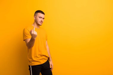 Genç ve yakışıklı bir adam kızgın, sinirli, asi ve agresif orta parmağını sallayarak düz arkaplana karşı savaşıyor.