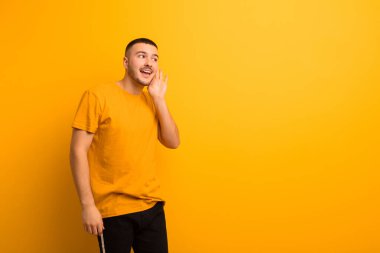 Genç yakışıklı adam gülümsüyor, tuhaf bir şekilde yan tarafa bakıyor, dedikoduları dinlemeye çalışıyor ya da düz arkaplanda bir sırra kulak misafiri oluyor.