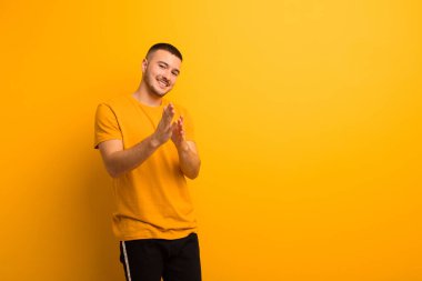 Genç yakışıklı adam kendini mutlu ve başarılı hissediyor, gülümsüyor ve alkışlıyor, düz arkaplan karşısında alkış tutarak tebrik ediyor.