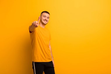 Genç yakışıklı adam gülümsüyor ve arkadaş canlısı görünüyor, bir numara ya da ilk eli önde, düz arkaplanda geriye doğru sayıyor.