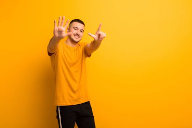 Genç yakışıklı adam gülümsüyor ve arkadaş canlısı görünüyor, 7 ya da 7 numarayı gösteriyor, elleri önde, düz arkaplanda geriye doğru sayıyor.