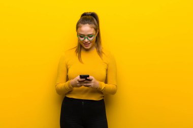 Sarı arka planda akıllı telefonu olan genç ve güzel bir kadın.