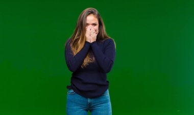 Genç ve güzel bir kadın mutlu ve kendinden emin, kamerayı iki eliyle gösteriyor ve gülüyor, yeşil arka planda seni seçiyor.