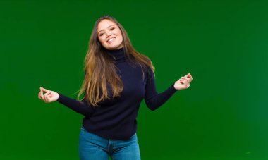 Genç, güzel bir kadın gülümsüyor, kaygısız hissediyor, rahat ve mutlu, dans ediyor ve müzik dinliyor, yeşil arka plandaki bir partide eğleniyor.