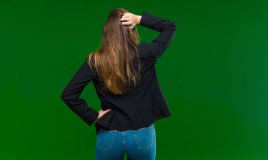 Genç, güzel bir kadın düşünüyor ya da şüphe ediyor, kafasını kaşıyor, şaşkın ve şaşkın hissediyor, yeşil arka planda ya da arka planda