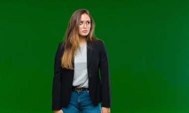 Genç, güzel bir kadın üzgün, üzgün ya da kızgın ve olumsuz bir tavırla, yeşil arka plana karşı anlaşmazlıkla bakıyor.
