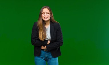 Genç, güzel bir kadın endişeli, hasta, hasta ve mutsuz hissediyor. Acılı bir mide ağrısı ya da yeşil arka planda grip geçiriyor.