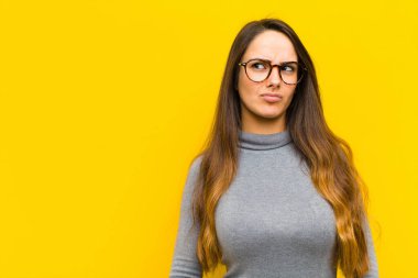 Genç ve güzel bir kadın şaşkın ve şaşkın görünüyor, merak ediyor ya da bir sorunu çözmeye çalışıyor ya da iş veya iş kavramı düşünüyor.