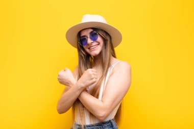 Genç, güzel bir kadın, neşeli bir şekilde gülümsüyor ve kutluyor. Yumruklarını sıkmış, kollarını kavuşturmuş, mutlu ve pozitif hissediyor.