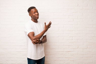 Genç Afrikalı Amerikalı siyahi adam, kafası karışık ve cahil hissediyor. Tuğla duvara karşı şüpheli bir açıklama ya da düşünceyi merak ediyor.