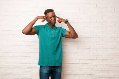 Genç Afro-Amerikan siyah adam ciddi ve konsantre görünümlü, beyin fırtınası yapıyor ve tuğla duvara karşı meydan okuyucu bir sorun düşünüyor.