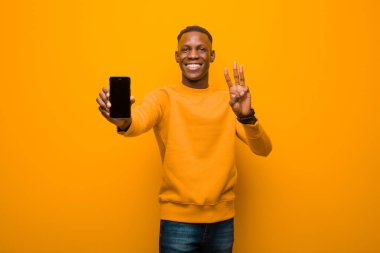 Genç Afro-Amerikan siyah adam turuncu duvara karşı akıllı bir telefonla
