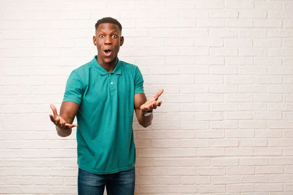 young african american black man feeling extremely shocked and surprised, anxious and panicking, with a stressed and horrified look against brick wall