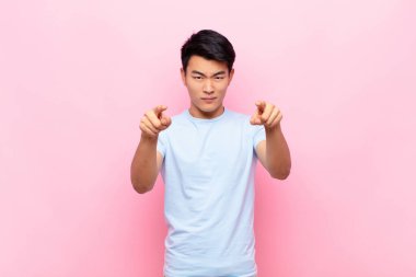 Genç Çinli adam kameraya hem parmaklarıyla hem de kızgın bir ifadeyle bakıyor. Düz duvarlara karşı görevini yapmanı söylüyor.