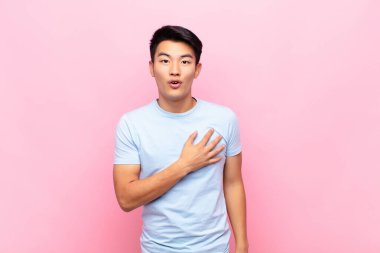 Genç Çinli adam şok olmuş ve şaşırmış hissediyor, gülümsüyor, el ele tutuşuyor, o olmaktan mutlu ya da düz renk duvarlara karşı minnettarlık gösteriyor.