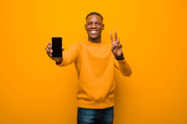 Genç Afro-Amerikan siyah adam turuncu duvara karşı akıllı bir telefonla