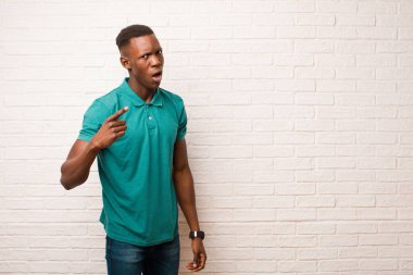 Genç Afrikalı Amerikalı siyahi adam kızgın agresif bir ifadeyle kameraya bakıyor. Tuğla duvara karşı öfkeli, çılgın bir patron gibi görünüyor.