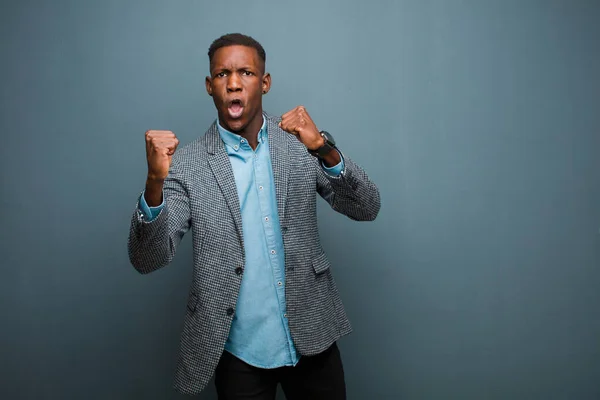 young african american black man celebrating an unbelievable success like a winner, looking excited and happy saying take that! against grunge wall