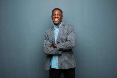 Genç Afro-Amerikan siyahi adam mutlu, gururlu ve tatmin olmuş görünüyor. Kollarını grunge duvarına dolamış gülümsüyor.