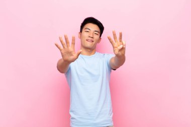 Genç Çinli adam gülümsüyor ve arkadaş canlısı görünüyor, 8 ya da 8 numarayı gösteriyor, düz renkli duvara doğru sayıyor.