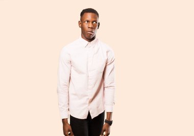 Genç Afrikalı Amerikalı siyah adam şok olmuş, mutlu, şaşırmış ve şaşırmış hissediyor, bej duvara karşı ağzı açık bir şekilde yan tarafa bakıyor.