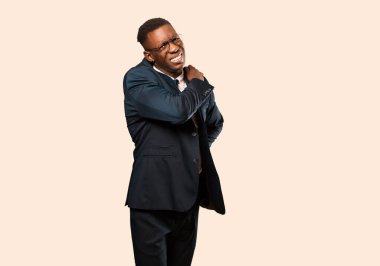 Afrikalı Amerikalı iş adamı yorgun, stresli, endişeli, hayal kırıklığına uğramış ve depresif hissediyor. Bej duvarda sırt ya da boyun ağrısı çekiyor.