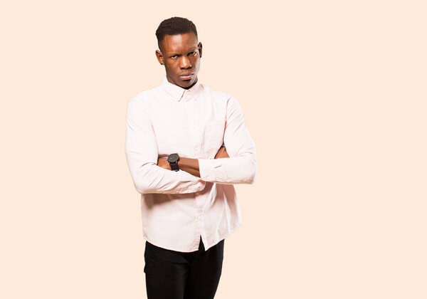 Young african american black man feeling displeased and disappointed, looking serious, annoyed and angry with crossed arms against beige wall