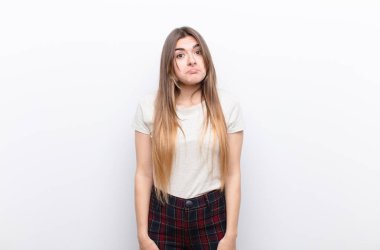 Genç, güzel bir kadın üzgün ve stresli. Kötü bir sürpriz yüzünden üzgün. Olumsuz, endişeli bir bakışla beyaz duvara bakıyor.