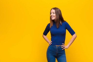 Genç kızıl saçlı kadın mutlu, neşeli ve kendinden emin görünüyor. Gururla gülümsüyor ve kalçalarını yassı duvara dayayıp iki elini de kullanmak istiyor.