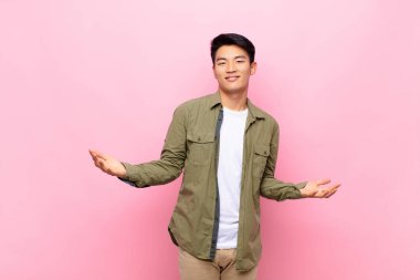 Genç Çinli adam mutlu, kibirli, gururlu ve kendinden memnun görünüyor. Düz renkli duvara karşı kendini bir numara gibi hissediyor.