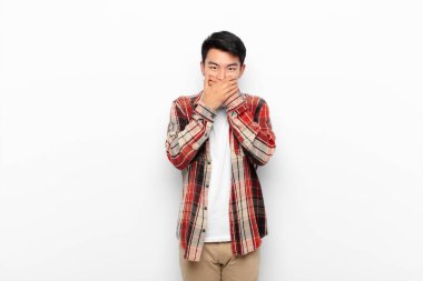 Genç Çinli adam şok olmuş, şaşırmış bir ifadeyle ağzını kapatıyor. Sır saklıyor ya da düz duvara karşı 