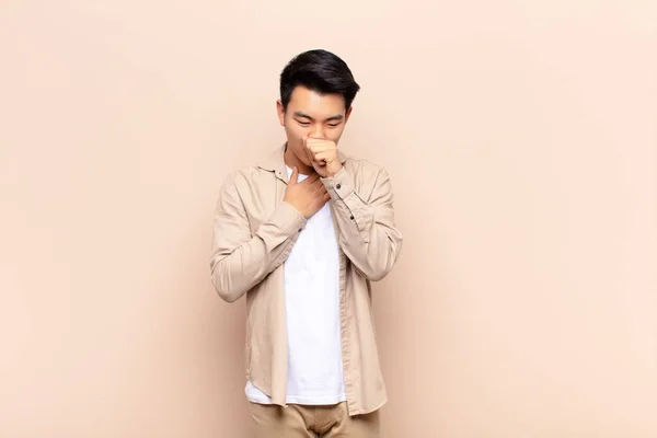 痛みを伴う喉やインフルエンザの症状を持つ若い中国人男性は 平らな色の壁に覆われた口で咳 — ストック写真