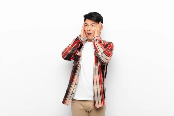若い中国人男性は フラットカラーの壁に直面して両手で側を見て 興奮し 驚いて感じている — ストック写真