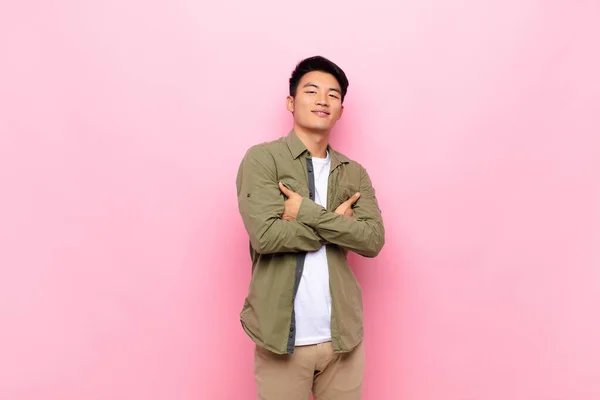 young chinese man laughing happily with arms crossed, with a relaxed, positive and satisfied pose against flat color wall
