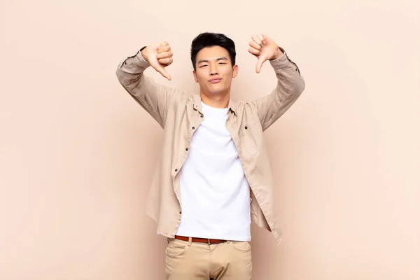 若い中国人男性は悲しい 失望した 怒っている 意見の相違に親指を示す 平らな色の壁に不満を感じる — ストック写真