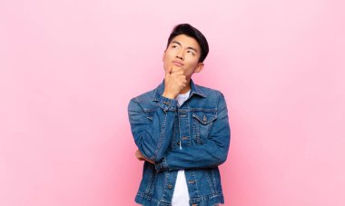 Genç Çinli adam düşünceli, meraklı ya da hayalperest hissediyor, hayal kuruyor ve düz renkli duvara karşı mekanı kopyalamak istiyor.