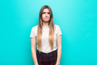 Genç ve güzel bir kadın kendini şaşkın ve kuşkulu hissediyor, merak ediyor ya da mavi duvara karşı karar vermeye çalışıyor.