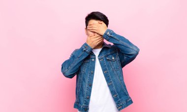 Genç Çinli adam kameraya hayır diyen iki eliyle yüzünü kapatıyor! Resimleri reddetmek ya da düz renkli duvara karşı resimleri yasaklamak