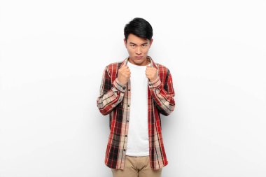 Genç Çinli, kendinden emin, sinirli, güçlü ve agresif görünüyor. Yumrukları boks pozisyonunda, düz renkli duvarlara karşı savaşmaya hazır.