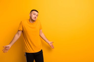 Genç, yakışıklı bir adam bilgisiz ve kafası karışık, hiçbir fikri yok, düz arkaplan karşısında aptal ya da aptal bir bakışla tamamen kafası karışmış.