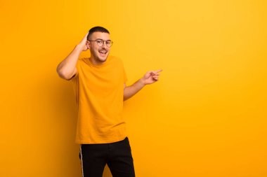 Genç yakışıklı adam gülüyor, mutlu, pozitif ve şaşırmış görünüyor, düz arkaplana karşı yanal fotokopi alanını işaret eden harika bir fikrin farkına varıyor.