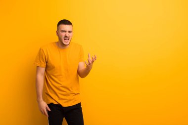 Genç yakışıklı adam sinirli, sinirli ve hayal kırıklığına uğramış görünüyor. Düz arkaplan karşısında senin neyin var? 